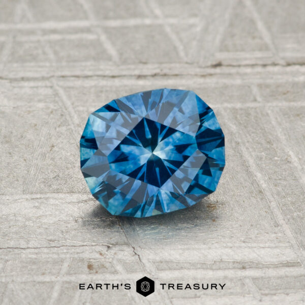 1.02-Carat Montana Sapphire (Heated) A 1.02-carat heated Montana sapphire gemstone is displayed on a textured gray surface with the "Earth's Treasury" logo and text at the bottom.
