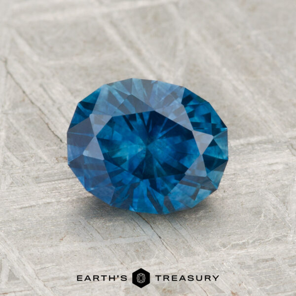 1.55-Carat Montana Sapphire (Heated) A 1.55-carat heated Montana sapphire is displayed on a textured gray surface with the text "EARTH'S TREASURY" below.