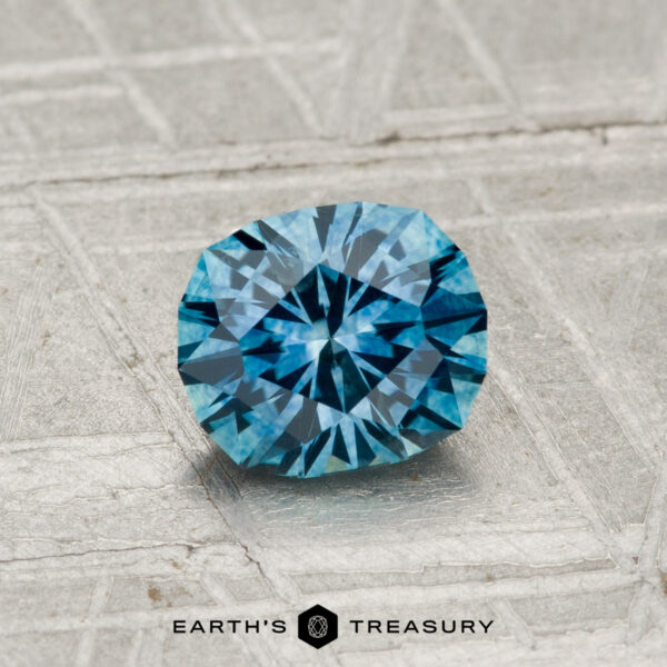 0.96-Carat Montana Sapphire (Heated) A 0.96-carat heated Montana sapphire rests on a textured metallic surface with "EARTH'S TREASURY" and a hexagon logo displayed below.