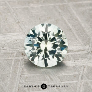 A 1.11-carat heated Montana sapphire, round brilliant-cut, showcased on a textured metallic surface with the "Earth's Treasury" logo at the bottom.