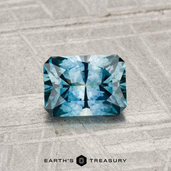 0.96-Carat Montana Sapphire (Heated) A 0.96-carat rectangular blue Montana sapphire (heated) with intricate facets rests on a textured light gray surface. The Earth's Treasury logo appears at the bottom of the image.