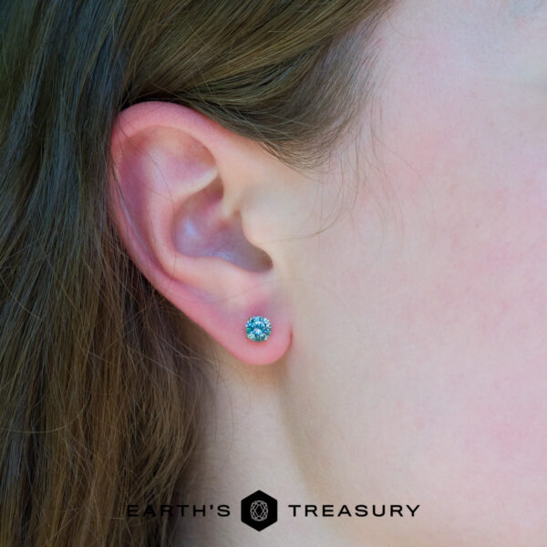 5.25 aqua blue Close-up of a person’s ear wearing a round, aqua blue "5.25 aqua blue" earring. The “Earth's Treasury” logo appears at the bottom of the image.