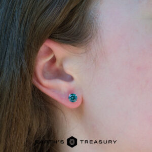 Close-up of a person's ear wearing a round teal blue 6.0 teal earring; "Earth's Treasury" logo appears at the bottom of the image.