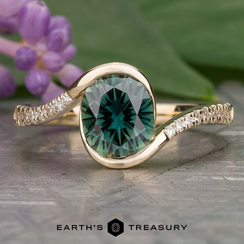Stacked from 15 images. Method=B (R=11,S=7) gold ring with a round green gemstone center and small diamonds on the band, shown on textured surface with a purple flower and green leaf in the background.