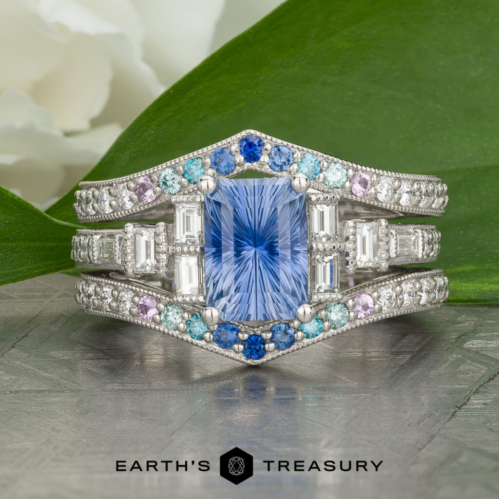 The "Stacked from 31 images. Method=B (R=14,S=2)" ring features a silver band with a rectangular blue gemstone center, accented by smaller blue, purple, and clear stones, shown on a metallic surface with green leaves in the background.
