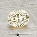 A 1.98-carat faceted light yellow oval Montana sapphire is displayed on a textured light gray surface with "EARTH'S TREASURY" at the bottom.