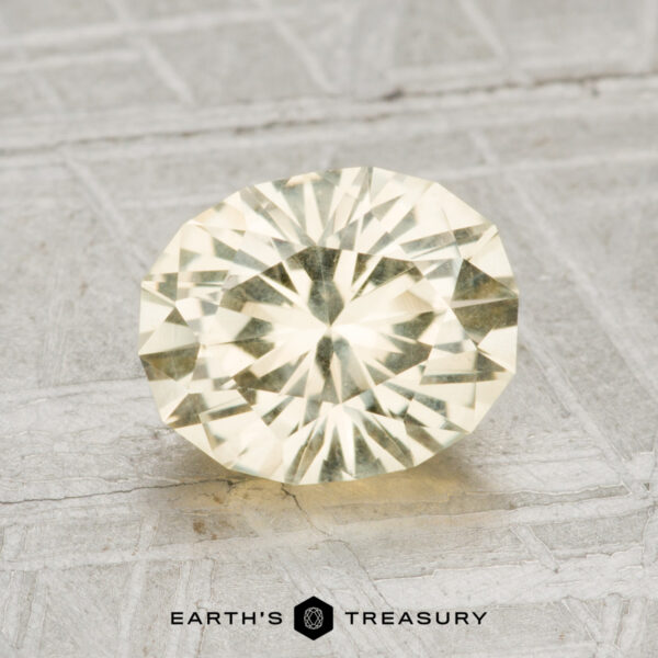 1.98-Carat Montana Sapphire A 1.98-carat faceted light yellow oval Montana sapphire is displayed on a textured light gray surface with "EARTH'S TREASURY" at the bottom.
