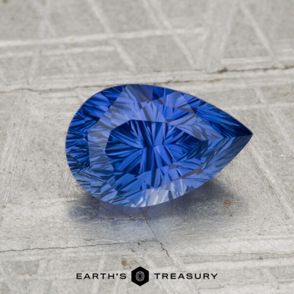 2.04-Carat Ceylon Sapphire A pear-shaped, vividly blue 2.04-carat Ceylon sapphire rests on a textured metallic surface with "EARTH'S TREASURY" at the bottom.