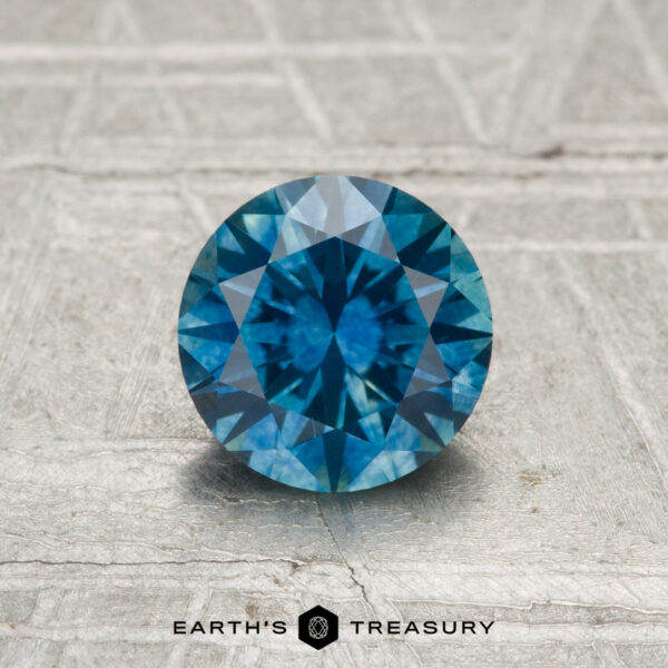 1.10-Carat Montana Sapphire (Heated) A round, blue 1.10-carat Montana Sapphire (Heated) rests on a textured, light-colored surface with "EARTH'S TREASURY" at the bottom.