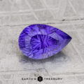 A 2.04-carat Ceylon sapphire, pear-shaped and faceted in purple, rests on a textured light gray surface with "EARTH'S TREASURY" below.