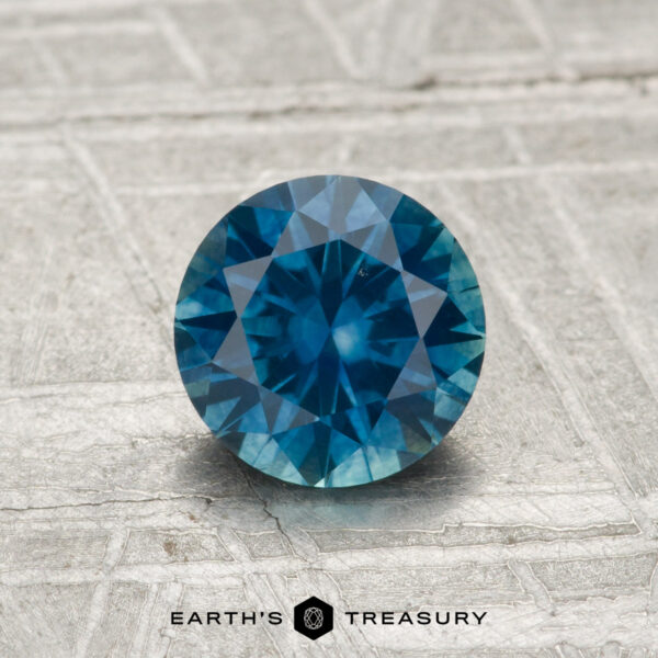 1.07-Carat Montana Sapphire (Heated) A 1.07-carat heated Montana sapphire with a round brilliant cut is displayed on a textured gray surface, with "EARTH'S TREASURY" at the bottom.