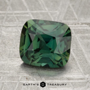 A 2.58-carat heated cushion-cut sapphire is showcased on a textured metallic background with “Earth’s Treasury” at the bottom.