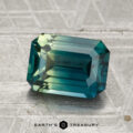 A 2.47-carat heated sapphire with an emerald cut in teal and green rests on a textured surface beside the Earth’s Treasury logo.