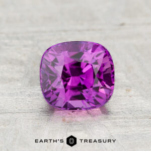 A 1.18-carat cushion-cut Ceylon sapphire (heated) is showcased on a textured gray surface with the "Earth's Treasury" logo below it.