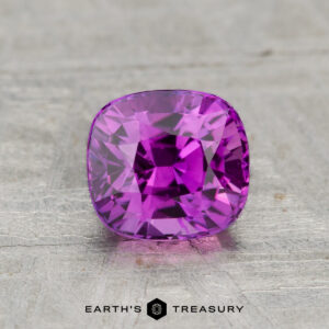 A 1.18-carat cushion-cut Ceylon sapphire (heated) is showcased on a textured gray surface with the "Earth's Treasury" logo below it.