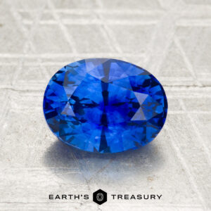 A 2.07-carat heated Ceylon sapphire, faceted in an oval shape, displayed on a textured surface with "Earth's Treasury" at the bottom.