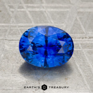 A 2.07-carat heated Ceylon sapphire, faceted in an oval shape, displayed on a textured surface with "Earth's Treasury" at the bottom.