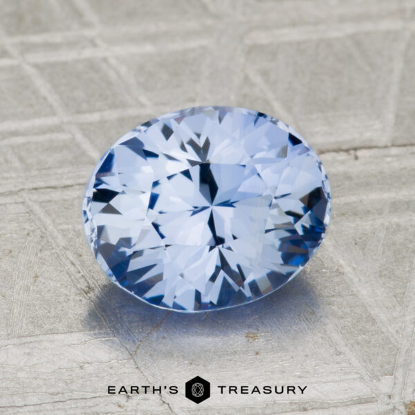 2.24-Carat Ceylon Sapphire A 2.24-carat Ceylon Sapphire, round brilliant-cut and blue, is displayed on a textured metallic surface with the "EARTH'S TREASURY" logo and text at the bottom.
