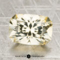A 4.87-carat Ceylon sapphire, cut in a rectangular faceted shape, rests on a textured gray surface with "Earth's Treasury" written below.