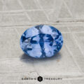 A 1.04-carat Ceylon Sapphire, faceted and oval-shaped, is displayed on a textured light gray surface with the "EARTH'S TREASURY" logo at the bottom.