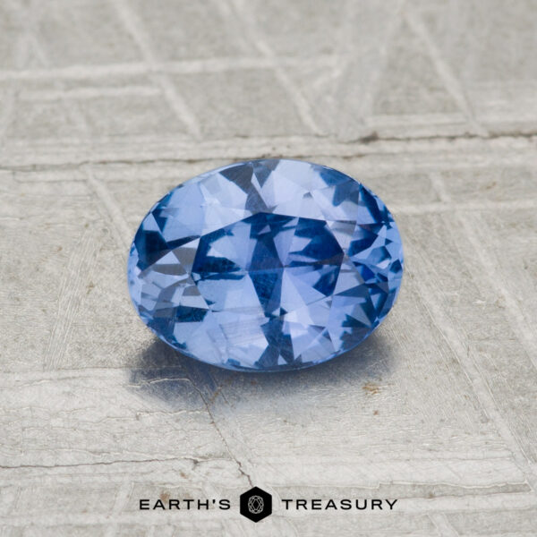 1.04-Carat Ceylon Sapphire A 1.04-carat Ceylon Sapphire, faceted and oval-shaped, is displayed on a textured light gray surface with the "EARTH'S TREASURY" logo at the bottom.