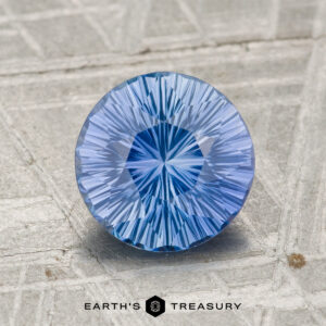 A round, faceted 1.89-carat Ceylon Sapphire gemstone is displayed on a textured gray surface with the text "Earth’s Treasury" at the bottom.