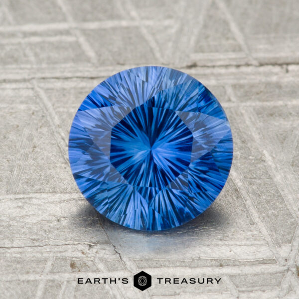 1.70-Carat Ceylon Sapphire (Heated) A 1.70-carat heated Ceylon sapphire, round and brilliant-cut, is showcased on a textured silvery surface with "Earth's Treasury" displayed at the bottom.