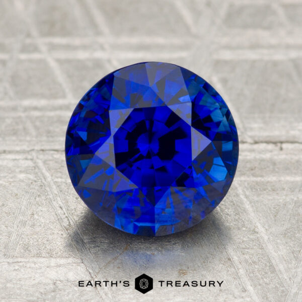 2.77-Carat Ceylon Sapphire (Heated) A 2.77-carat heated Ceylon sapphire, round brilliant-cut, sits on a textured metallic surface with "EARTH'S TREASURY" visible below.