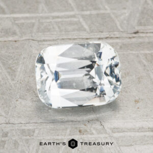 A 2.03-carat heated Ceylon sapphire, cut in a rectangular cushion shape, is showcased on a textured gray surface with "EARTH'S TREASURY" at the bottom.