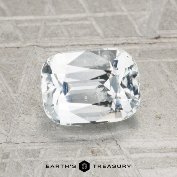2.03-Carat Ceylon Sapphire (Heated) A 2.03-carat heated Ceylon sapphire, cut in a rectangular cushion shape, is showcased on a textured gray surface with "EARTH'S TREASURY" at the bottom.