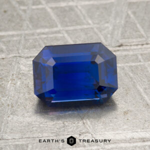 A 2.02-carat Ceylon Sapphire, cut in a rectangular faceted shape and displayed on a textured surface, with the text "Earth's Treasury" beneath it.
