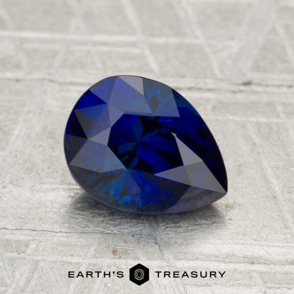 1.96-Carat Madagascar Sapphire (Heated) A 1.96-carat Madagascar sapphire (heated), pear-shaped and blue, rests on a textured gray surface with the text "EARTH'S TREASURY" below.