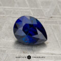 A 1.96-carat Madagascar sapphire (heated), pear-shaped and blue, rests on a textured gray surface with the text "EARTH'S TREASURY" below.