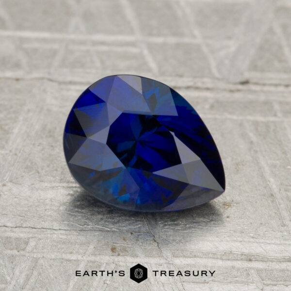 1.96-Carat Madagascar Sapphire (Heated) A 1.96-carat Madagascar sapphire (heated), pear-shaped and blue, rests on a textured gray surface with the text "EARTH'S TREASURY" below.