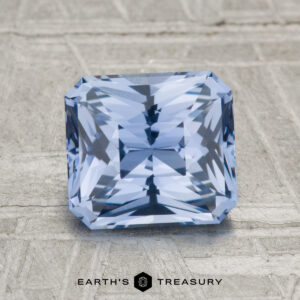 A 2.32-carat Ceylon sapphire, square-cut with intricate facets, rests on a textured gray surface. The "EARTH'S TREASURY" logo and text are featured at the bottom.