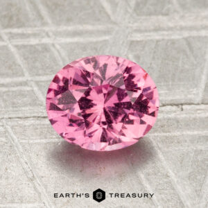 A round, faceted 1.56-carat Madagascar pink sapphire is displayed on a textured gray background with the words "Earth's Treasury" at the bottom.