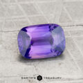 A 1.51-carat Ceylon sapphire, faceted and rectangular in shape with a rich purple hue, rests on a textured gray surface. “Earth’s Treasury” appears at the bottom.
