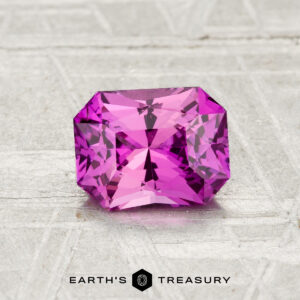 A rectangular-cut, vivid pink 1.31-carat heated Ceylon sapphire is displayed on a textured surface with "Earth's Treasury" text at the bottom.