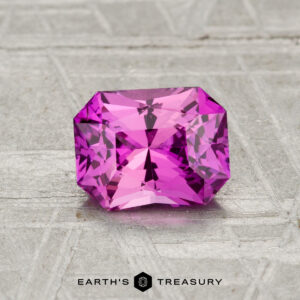 A rectangular-cut, vivid pink 1.31-carat heated Ceylon sapphire is displayed on a textured surface with "Earth's Treasury" text at the bottom.