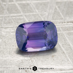 A 1.51-carat Ceylon sapphire, cushion-cut and purple, is shown on a textured silver-gray surface with the text "EARTH'S TREASURY" below.