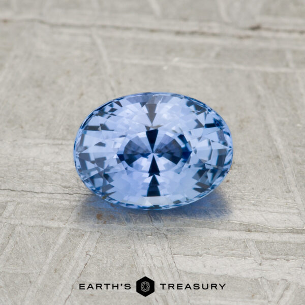 1.11-carat Ceylon sapphire, oval-cut and blue, displayed on a textured gray surface with "EARTH'S TREASURY" text at the bottom.
