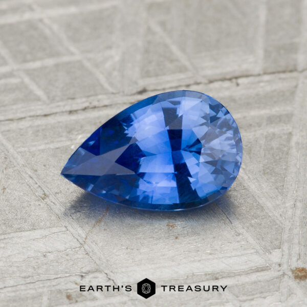 1.12-Carat Ceylon Sapphire in a pear shape, blue hue, shown on a textured gray surface with the "Earth's Treasury" logo at the bottom.