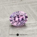 A 1.09-carat, oval-cut Montana sapphire with a light purple hue is displayed on a textured gray surface, with "EARTH'S TREASURY" written below.