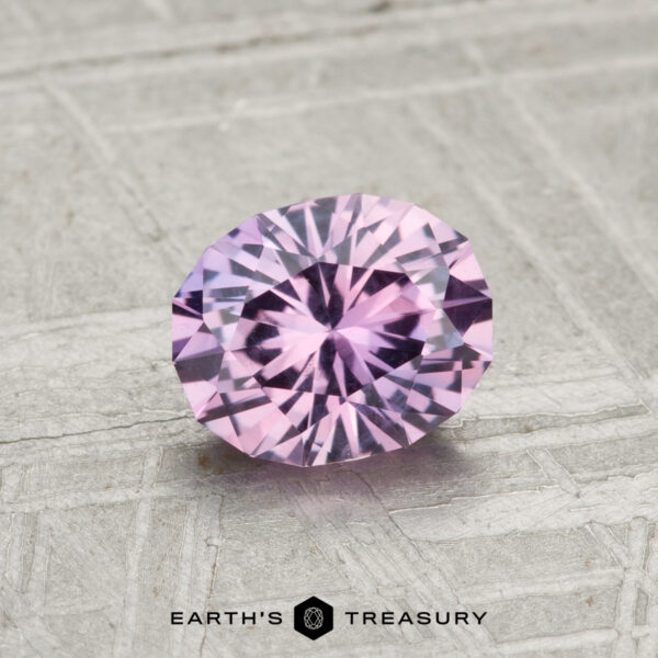 1.09-Carat Montana Sapphire A 1.09-carat, oval-cut Montana sapphire with a light purple hue is displayed on a textured gray surface, with "EARTH'S TREASURY" written below.