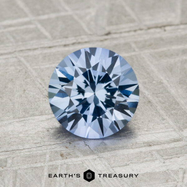 1.37-Carat Ceylon Sapphire A 1.37-carat Ceylon sapphire, round brilliant-cut and blue, is displayed on a textured gray surface with the text "Earth's Treasury" below.