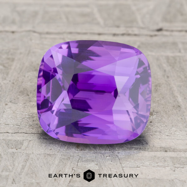 3.06-Carat Ceylon Sapphire A 3.06-carat Ceylon sapphire, cushion-cut and purple, displayed on a light textured surface with the text "EARTH'S TREASURY" at the bottom.