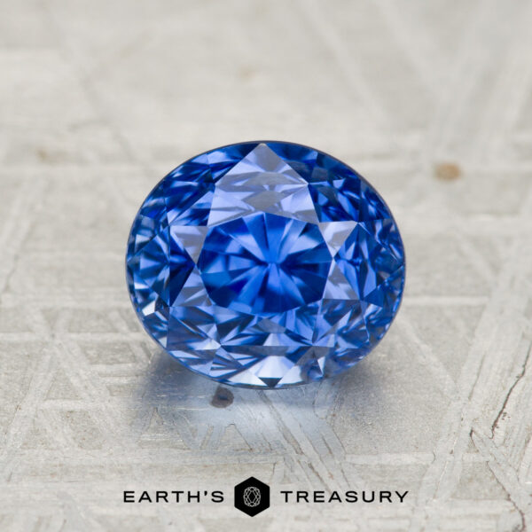 A 2.27-carat heated Ceylon sapphire, round brilliant-cut, displayed on a patterned metallic surface with the text "EARTH'S TREASURY" below.