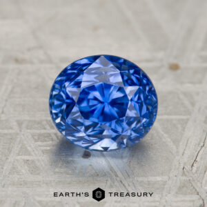 A 2.27-carat heated Ceylon sapphire, round brilliant-cut, displayed on a patterned metallic surface with the text "EARTH'S TREASURY" below.