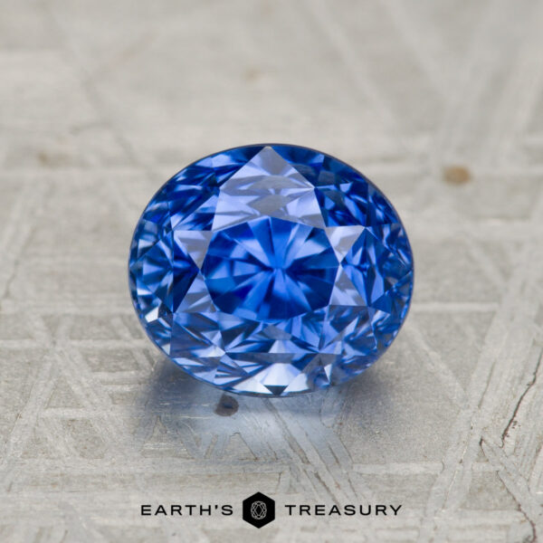 2.27-Carat Ceylon Sapphire (Heated) A 2.27-carat heated Ceylon sapphire, round brilliant-cut, displayed on a patterned metallic surface with the text "EARTH'S TREASURY" below.