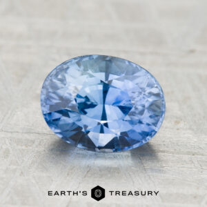 2.49-carat Ceylon Sapphire (heated), oval-cut and blue, showcased on a textured gray surface with "Earth's Treasury" displayed at the bottom.